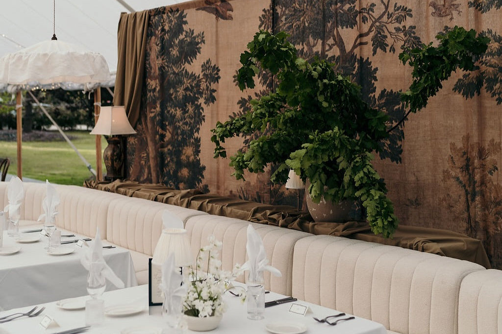Decorative setup with tables, chairs, and floral arrangements under a tent.