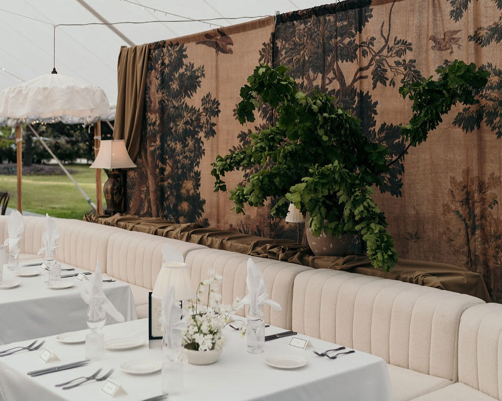 Decorative setup with tables, chairs, and floral arrangements under a tent.