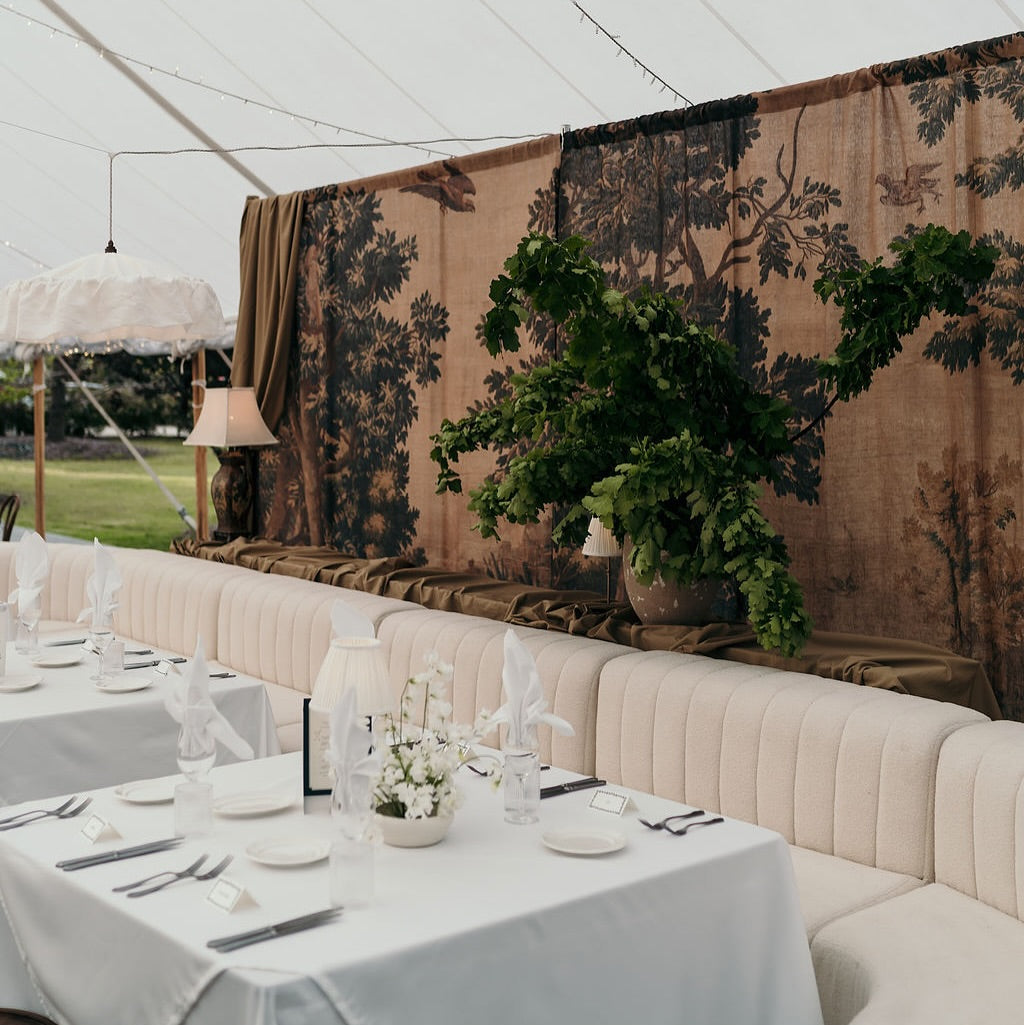 Decorative setup with tables, chairs, and floral arrangements under a tent.